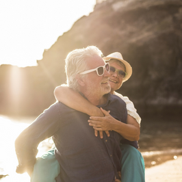 woman on the back of a man, both smiling and wearing sunglasses on the beach