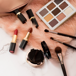 makeup spread out over a light pink blanket and countertop